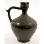 A MIDDLE EASTERN BLACK GLAZED EARTHENWARE PUZZLE JUG WITH TRI-LOBED LIP AND INCISED DECORATION, 31CM