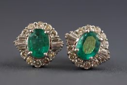 A modern white metal pair of stud earrings each set with an oval emerald