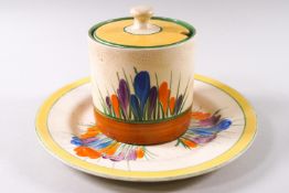 A Clarice Cliff Spring crocus pattern covered cylindrical jam pot, 7cm high and similar plate,