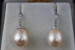 A modern white metal pair of pearl and diamond drop earrings.