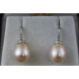 A modern white metal pair of pearl and diamond drop earrings.