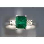 A modern white metal three stone ring set with a rectangular emerald.