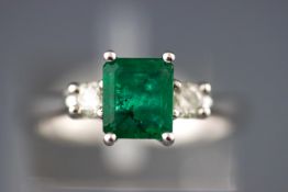 A modern white metal three stone ring set with a rectangular emerald.