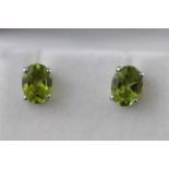 A modern white metal pair of single stone studs, each set with an oval faceted cut peridot.