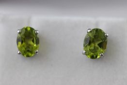 A modern white metal pair of single stone studs, each set with an oval faceted cut peridot.