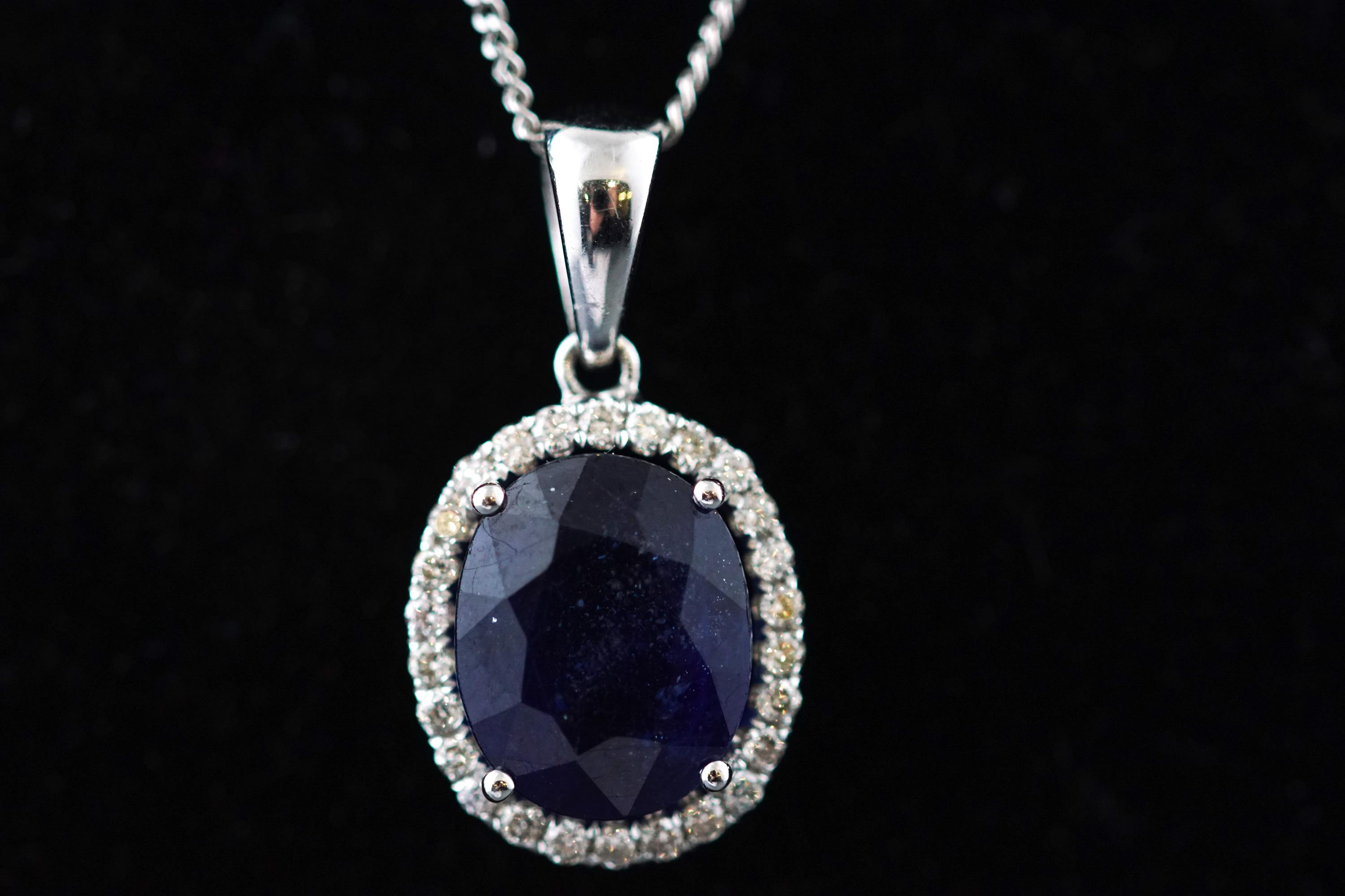 A modern white metal cluster pendant set with an oval faceted sapphire* and surrounded by diamonds.