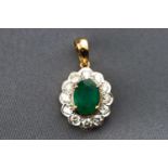 A modern yellow metal cluster pendant set with an oval faceted cut emerald