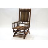 A Victorian hardwood and upholstered rocking chair with padded arms on baluster supports
