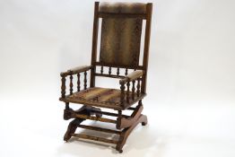 A Victorian hardwood and upholstered rocking chair with padded arms on baluster supports