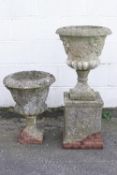 A pair of composite stone campana form garden urns, one on a squared socle,