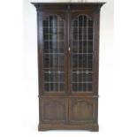 An oak arts and crafts style bookcase with two panel door cupboard base and glazed leaded doors