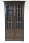 An oak arts and crafts style bookcase with two panel door cupboard base and glazed leaded doors