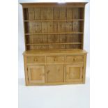 A pine dresser in two sections, the top with a plain cornice with three shelves,