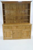 A pine dresser in two sections, the top with a plain cornice with three shelves,