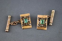 A yellow metal pair of cufflinks each set with a rectangular emerald