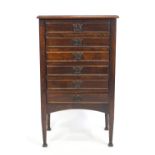 A stained wood music cabinet of upright rectangular form with plain top over six fall front drawers