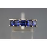 A white metal dress ring set with five square faceted synthetic sapphires.