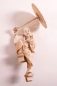 A Japanese Meiji period ivory okimono carving of a man with an umbrella,