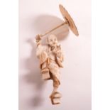 A Japanese Meiji period ivory okimono carving of a man with an umbrella,