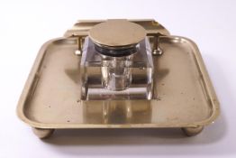 A brass ink bottle stand with pen rest, raised on four ball feet,