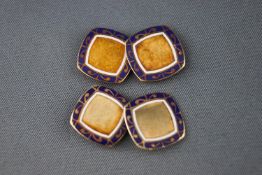 A pair of yellow metal cufflinks. Finished with a scroll design with white and blue enamel.