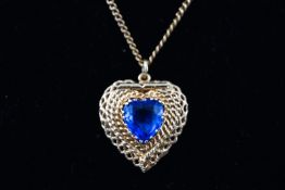 A yellow metal filigree locket pendant set with a heart cut dark blue paste stone.