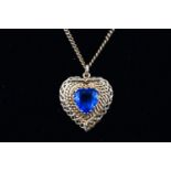 A yellow metal filigree locket pendant set with a heart cut dark blue paste stone.