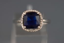 A white metal cluster ring set with a cushion cut synthetic sapphire