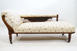 An Edwardian chaise longue with a hardwood frame carved with floral motifs and ribbed panels and