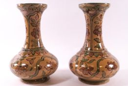 A pair of early 20th century Persian pottery vases, each decorated with flowers on a beige ground,