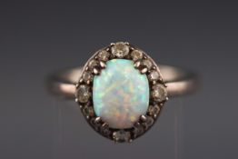 A white metal cluster ring set with synthetic opal cabochon and cubic zirconias.