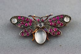 A yellow metal butterfly brooch set with cabochon moonstones and rubies. Pin and clip fitting.