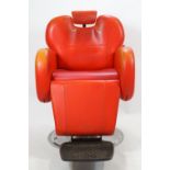 A retro red leather barbers chair of robust form with raising mechanisms and neck rests,