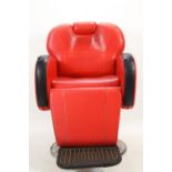 A retro red leather barbers chair of robust form with raising mechanisms and neck rests,