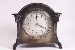 A Kendal & Dent mantle clock in arched metal case enclosing an enamel dial,