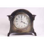 A Kendal & Dent mantle clock in arched metal case enclosing an enamel dial,