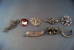 A collection of eight white metal brooches of variable designs.