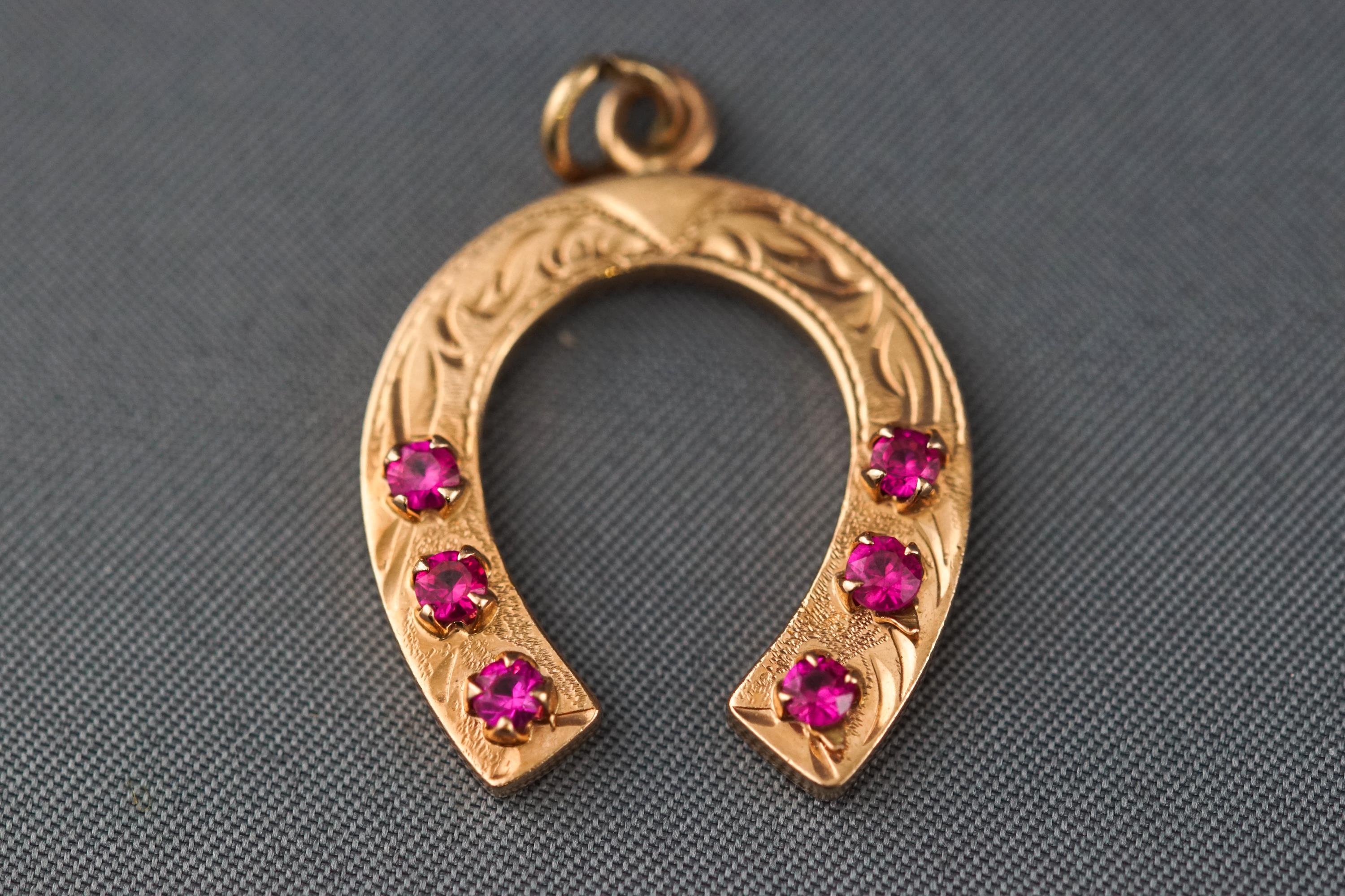 A yellow metal engraved horseshoe pendant set with six synthetic rubies. Stamped 585 for 14ct gold.