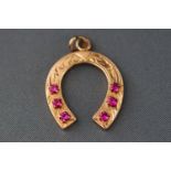 A yellow metal engraved horseshoe pendant set with six synthetic rubies. Stamped 585 for 14ct gold.
