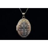 A yellow metal oval picture locket with embossed design suspended form a fine link curb chain.