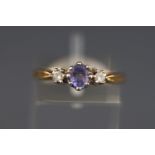 A yellow metal ring set with an oval tanzanite and two round brilliant cut diamonds,