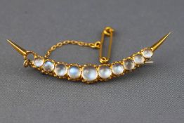 A yellow metal crescent brooch set with graduated cabochon cut moonstones.