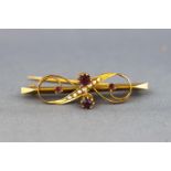 A yellow metal bar brooch of scroll design set with rhodolite garnet (untested) and seed pearls.