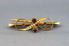 A yellow metal bar brooch of scroll design set with rhodolite garnet (untested) and seed pearls.