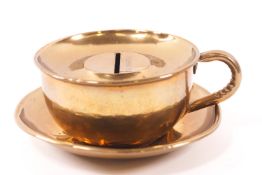 A brass novelty money box in the form of a tea cup,