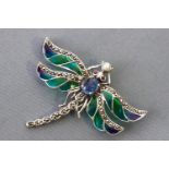 A white metal dragonfly brooch with green enamelled wings and set with a blue cabochon sapphire...