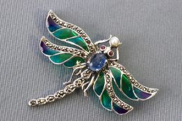 A white metal dragonfly brooch with green enamelled wings and set with a blue cabochon sapphire...