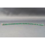 A white metal line bracelet set with twenty six oval faceted cut emeralds...