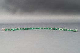 A white metal line bracelet set with twenty six oval faceted cut emeralds...