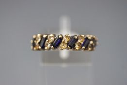 A yellow metal half hoop ring set with synthetic blue sapphires and colourless paste stones.